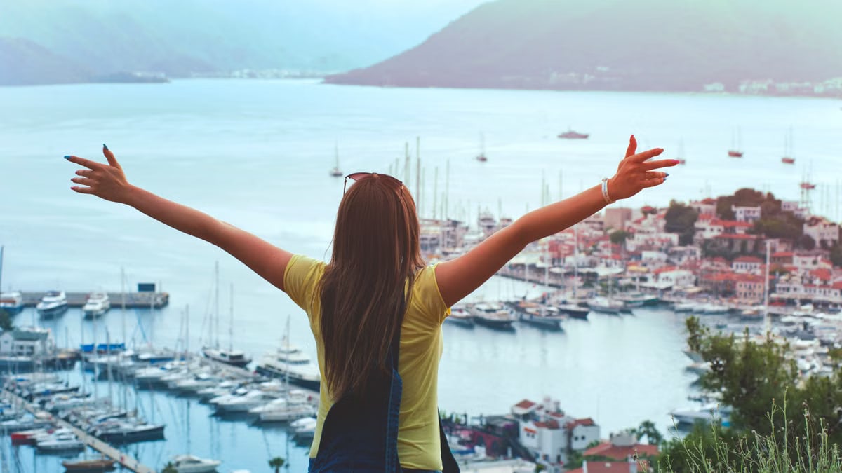 A woman with open arms enjoys a scenic summer view of Marmaris harbor and yachts.